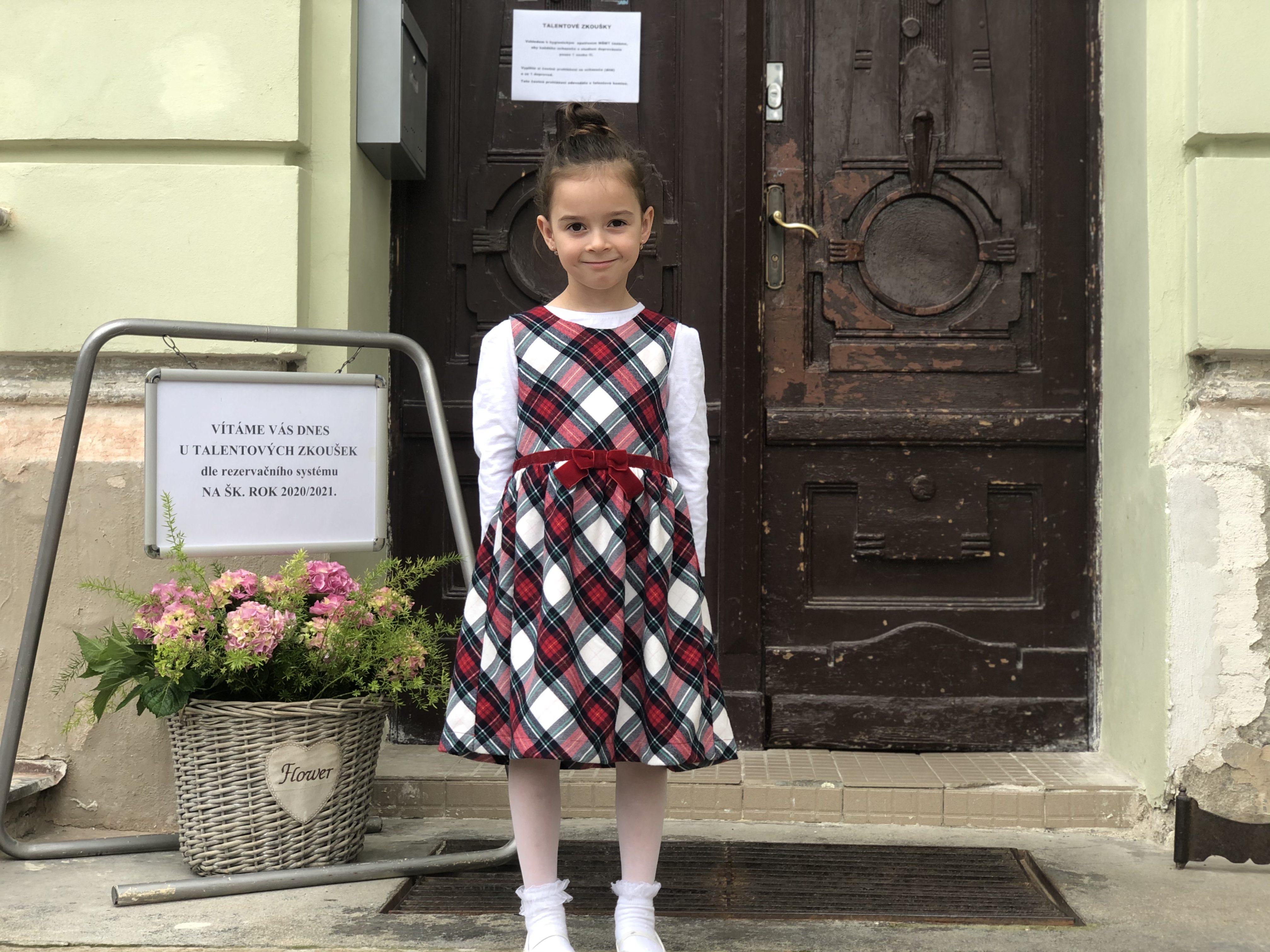 Holčička se chystá na talentové zkoušky, stojí před budovou ZUŠ u uvítací cedule